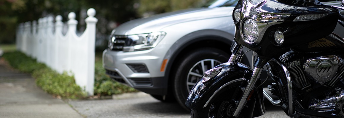 A silver SUV and a black motorcycle sit in a driveway next to a white picket fence.
