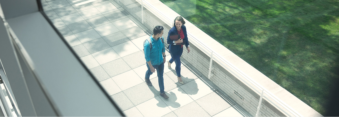 Two employees in conversation walk on a paved path next to grass at Progressive Corporate Headquarters.