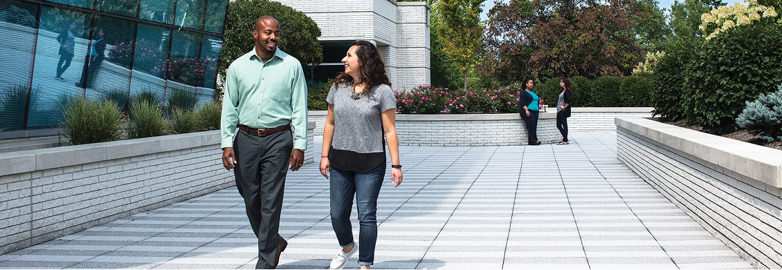 Two employees in conversation walk on an outside walkway at Progressive Corporate Headquarters.