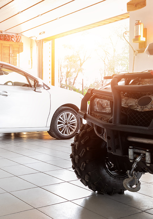 A white sedan next to a four by four parked in a garage.