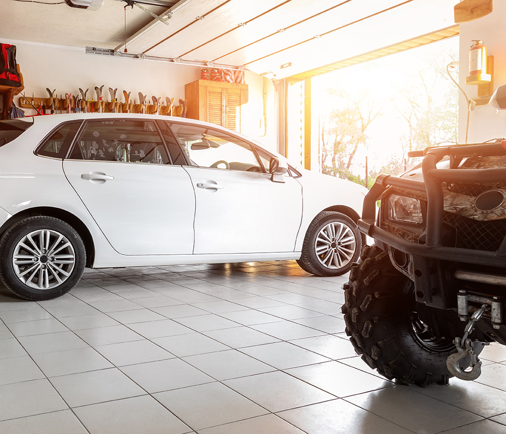 A white sedan next to a four by four parked in a garage.