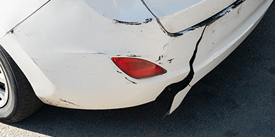 The bumper of a white car with damage on its back left bumper.